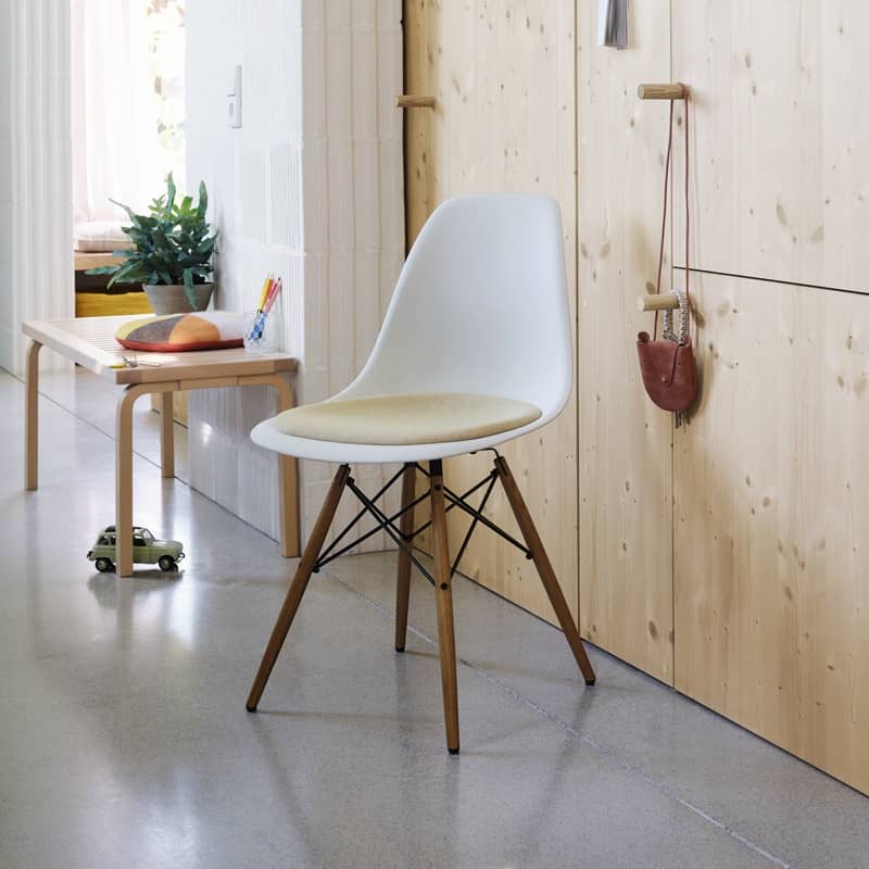 Ein Eames Plastic Chair mit Holzf&uuml;ssen steht vor einem h&ouml;lzernen Schrank